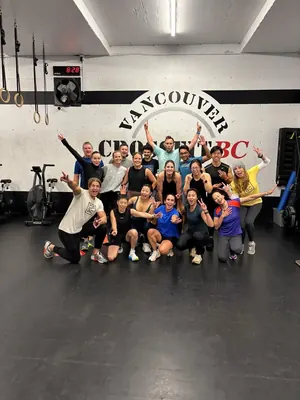 CrossFit BC members celebrating with peace signs in front of the gym wall logo