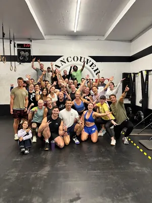 Large CrossFit BC class group photo cheering under the Vancouver CFBC wall logo