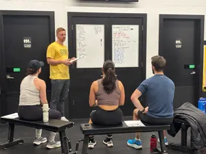 CrossFit BC coach in a yellow CFBC tee briefing members at the workout whiteboard