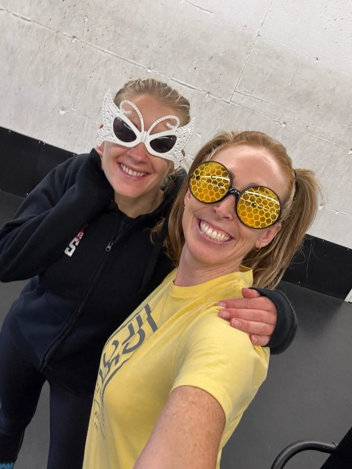Two CrossFit BC members in colourful party sunglasses smiling on the gym floor