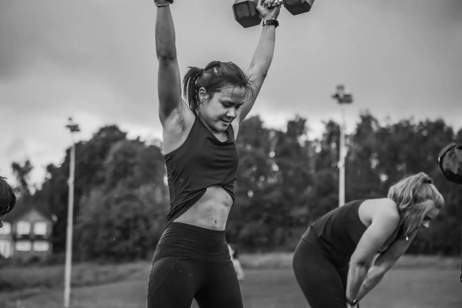 Female athlete pressing a dumbbell overhead during a Deadly Dozen labour